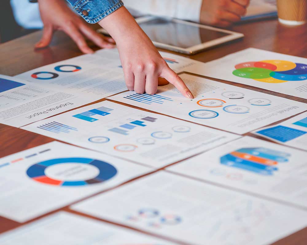 A finger is pointing to some data on a piece of paper, while other sheets of paper are laid out around it.